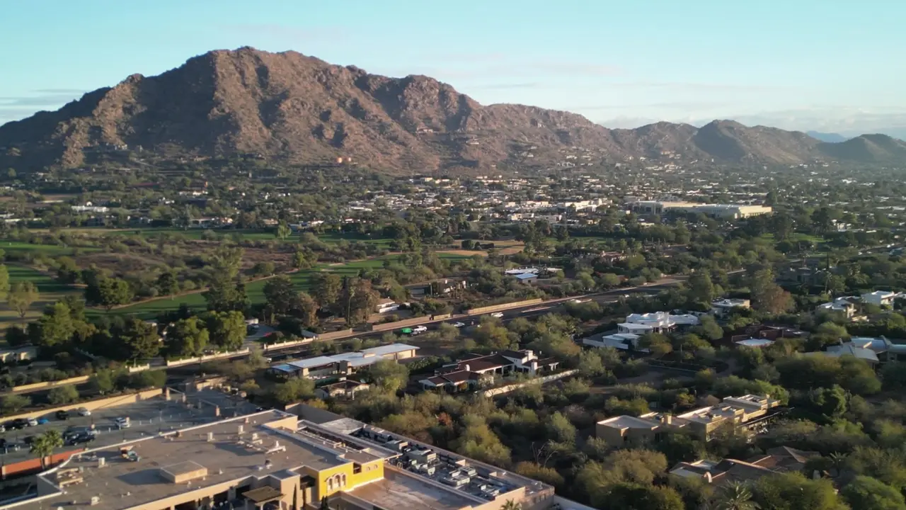 Aerial view of Arcadia neighborhood homes and trees below Camelback Mountain at golden hour